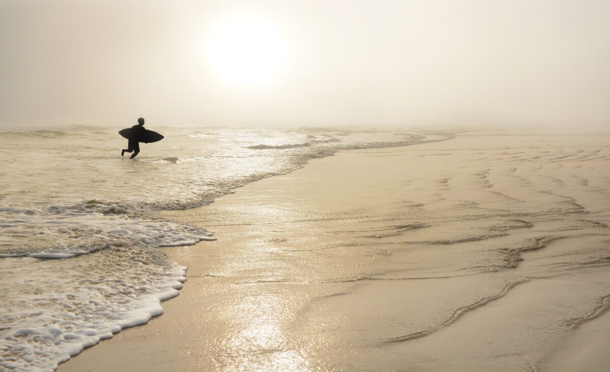 Boy running with surfboard on a golden beach at sunrise.