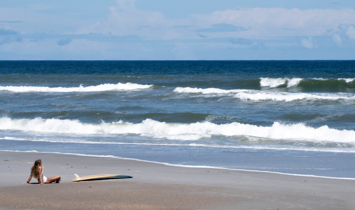 Back of girl sitting on beach with surfboard, Vilano Beach Florida
