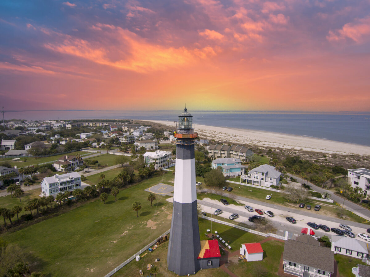 Aerial shot of the a gorgeous spring landscape at Tybee Island Beach with the lighthouse, blue ocean water, a brown sandy beach, homes and lush green trees and grass in Tybee Island Georgia USA
