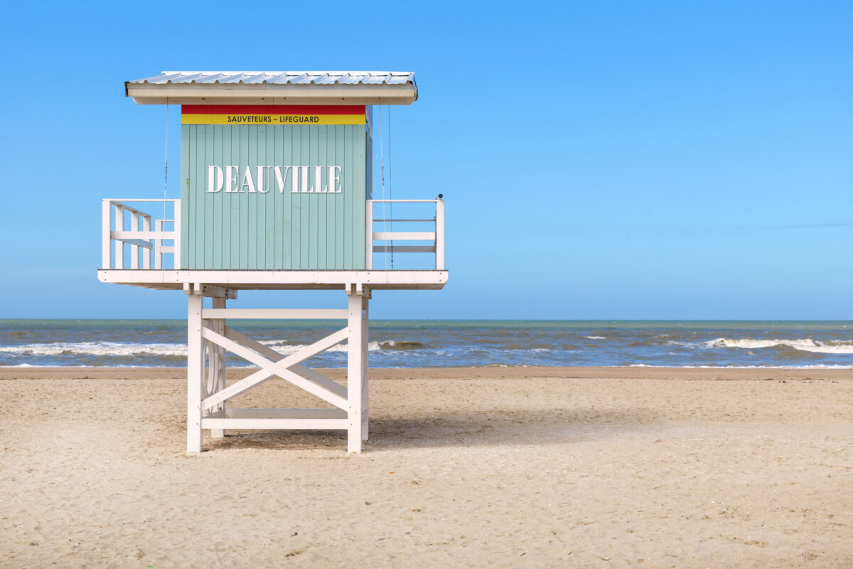 Spring Deauville beach with lifeguard station shows complete solitude, solitude extending across empty sand and calm water, solitude creating reflective and serene coastal mood