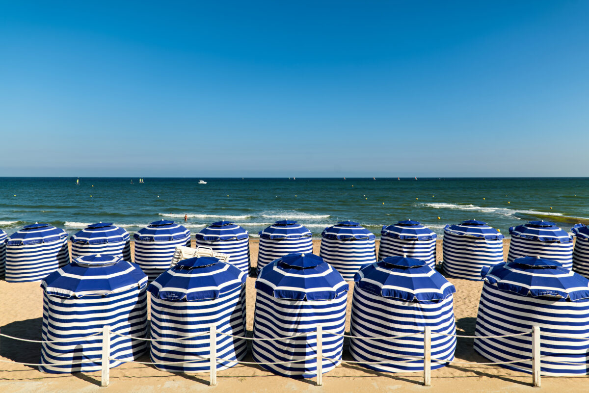 Beach scene in Cabourg Normandy with striped umbrellas on sand. Many striped umbrellas are set up on the beach in Cabourg, Normandy. People can be seen enjoying the sun and sea in the background