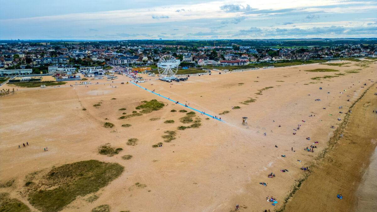 Panoramic aerial view of the seaside town of Ouistreham in Normandy. Wide sandy beach with a Ferris wheel and the town in the background, capturing the summer holiday