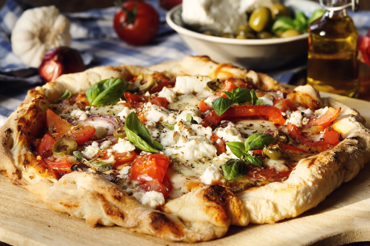 Hearty greek style pizza with feta cheese, olives, red onions, tomatoes, garlic and basil leaves
