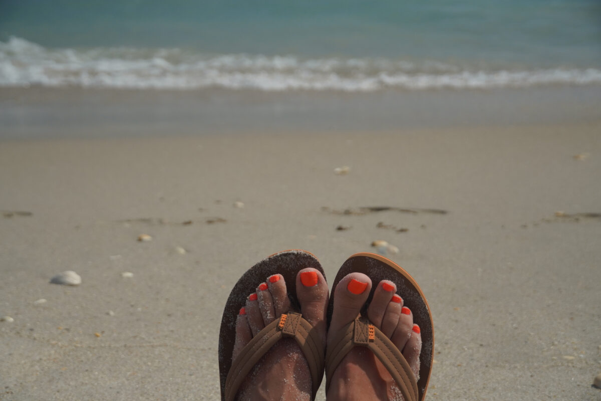 Tan Colored Reef Flip Flops with sand and ocean in background_Brandy Jo Hastings