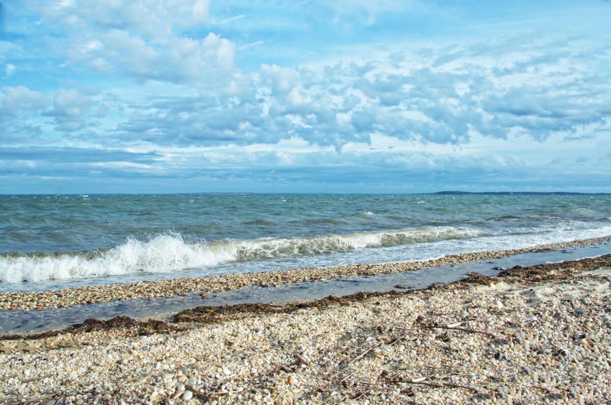 View of Gardiners Bay From Orient Beach State Park, Long Island, NY. Looking to the southeast. Orient Beach State Park is at the tip of the northern shore of Long Island. The waves crash on a pebble beach, whilte overhead grey and white clouds form over a blue sky. Picture taken in late afternoon in early summer.