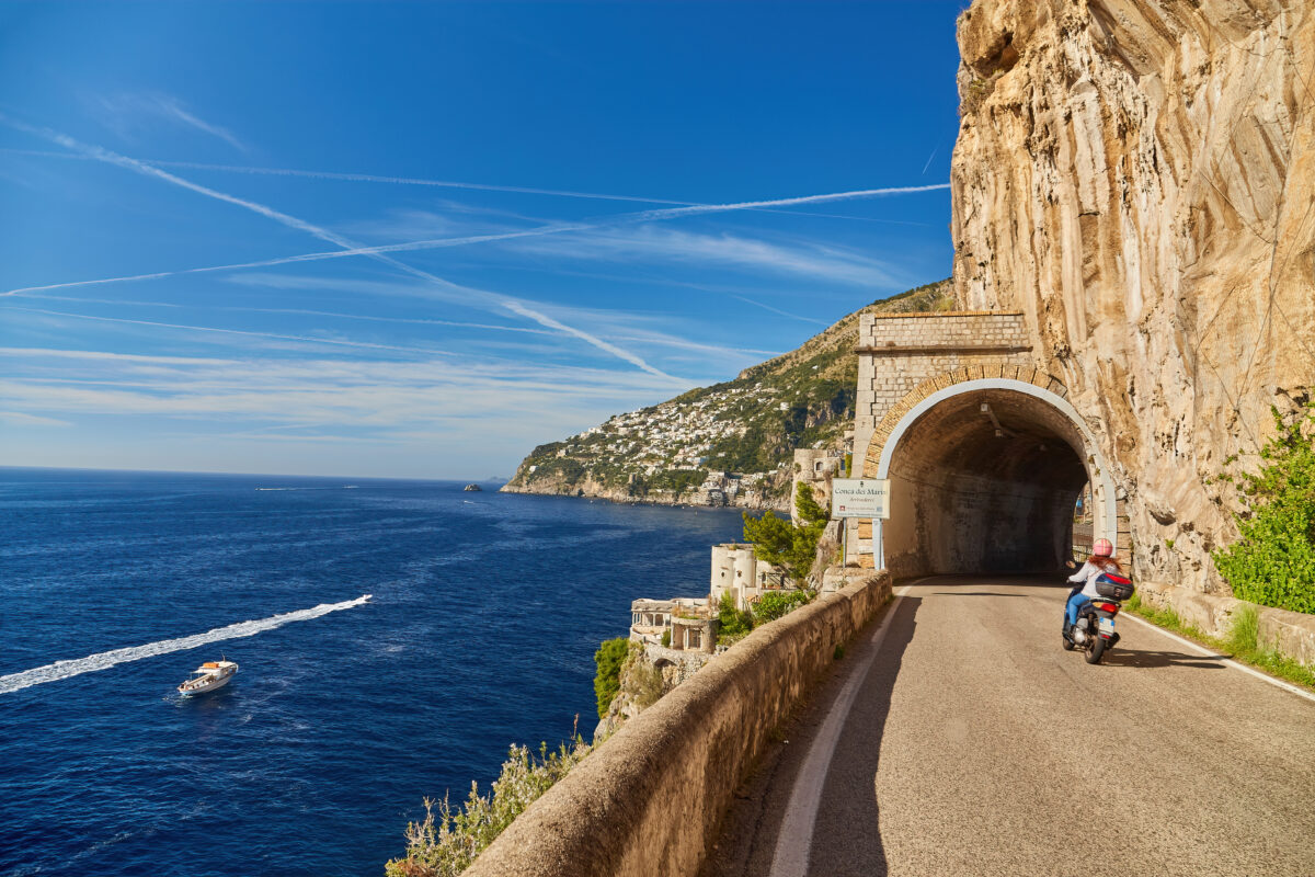 Scooter drives along the road along the Amalfi coast, approaching the tunnel Conca dei Marini, Italy