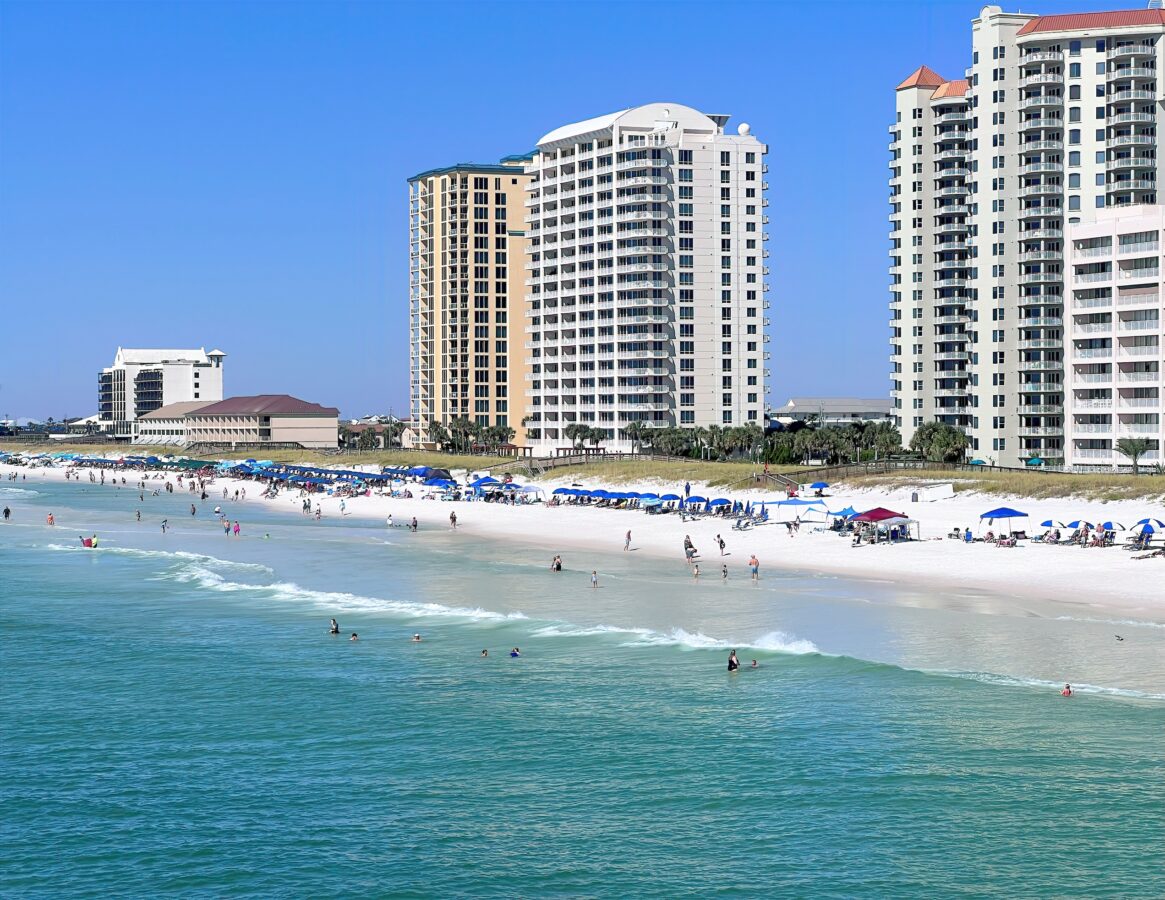 Navarre, Florida, Beach and Condos. Navarre Beach in Florida features a pristine stretch of white granite sand, with people enjoying the beach under a clear blue sky, while nearby condos add to the scenic coastal view.